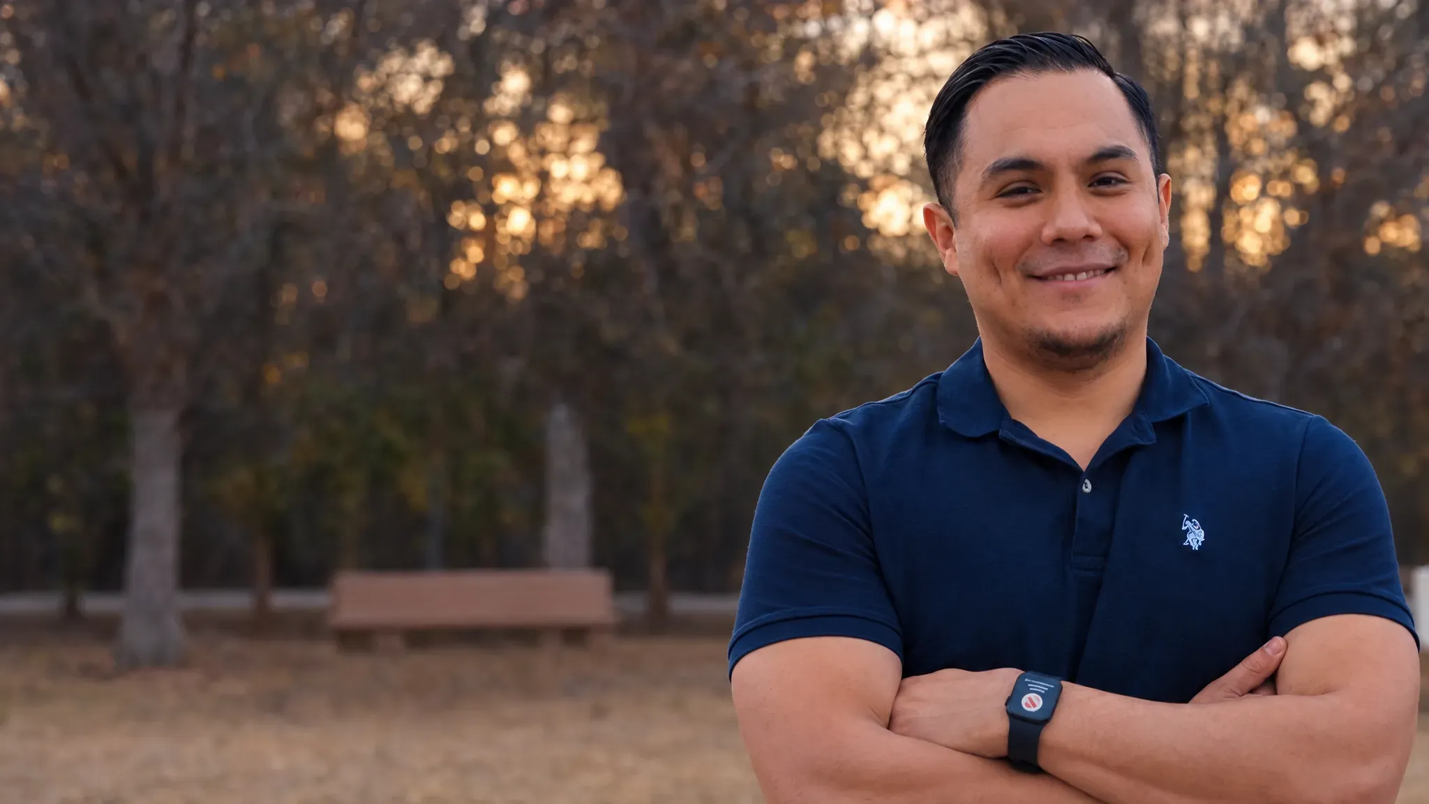 Juan Estrada sonriendo con los brazos cruzados en un parque de Gwinnett al atardecer
